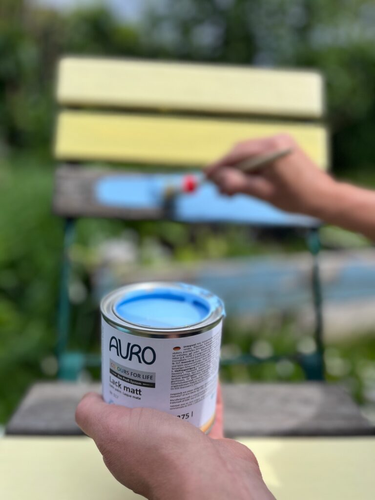 Dose mit blauem Lack von AURO vor einem Gartenstuhl