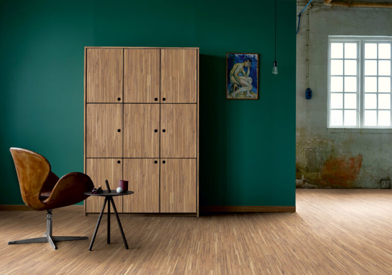 leerer Raum mit Wand in petrol und Holzboden in Stäbchenoptik, an Wand steht ein Schrank ebenfalls in Stäbchenoptik
