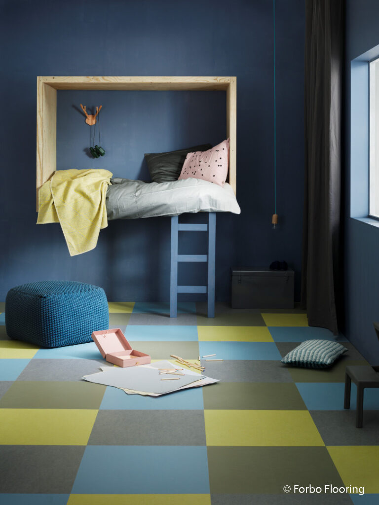 leeres Kinderzimmer mit kariertem Boden in blau und grün, blaue Wände, an Wand hängt ein großer Rahmen, in dem man sitzen kann
