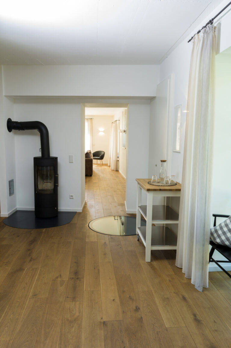 Eingangsbereich mit Holzofen und kleinem Regal mit Gläsern und Karaffe, Abgang in zwei weitere Zimmer