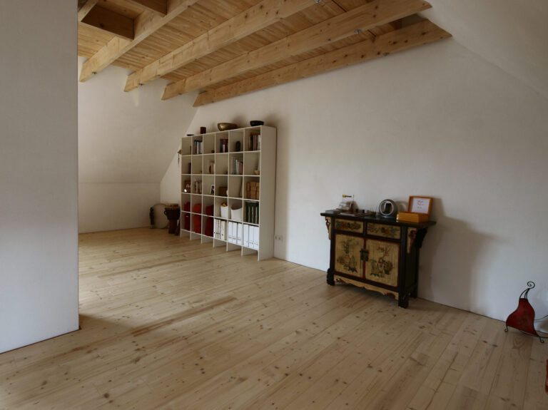 leeres Dachgeschoss mit Holzboden in Fichte und Holzdecke, kleine Bauern-Kommode, modernes Bücherregal, orientalische Lampe