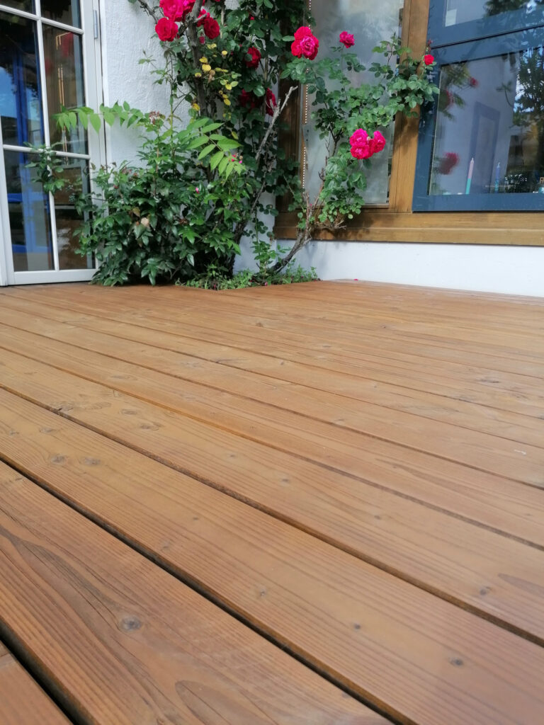 Holzterrasse mit Rose im Hintergrund