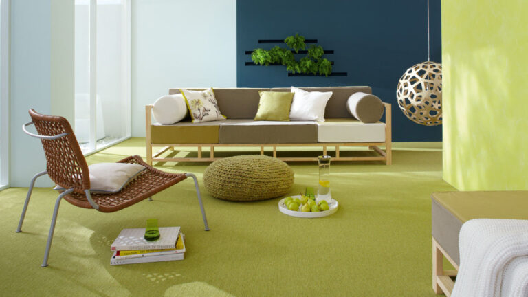 grüner Teppich mit grün-weißem Sofa, grün-blauen Wänden, grünem Bodenkissen und Korbsessel
