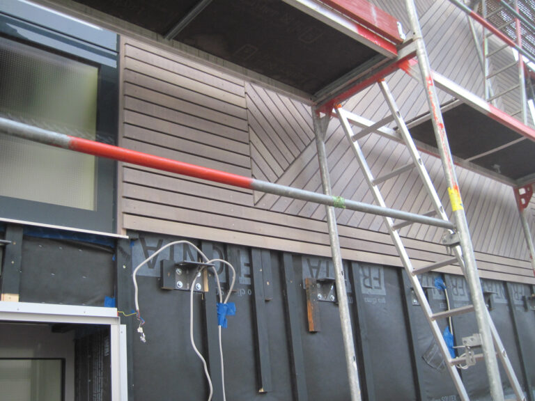 Detailansicht einer Fassade mit Gerüst, an die eine Holzverkleidung angebracht wird