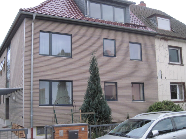 Außenansicht eines Doppelhauses, linke Hälfte frisch renoviert mit Holzverkleidung, rechts noch mit altem Putz