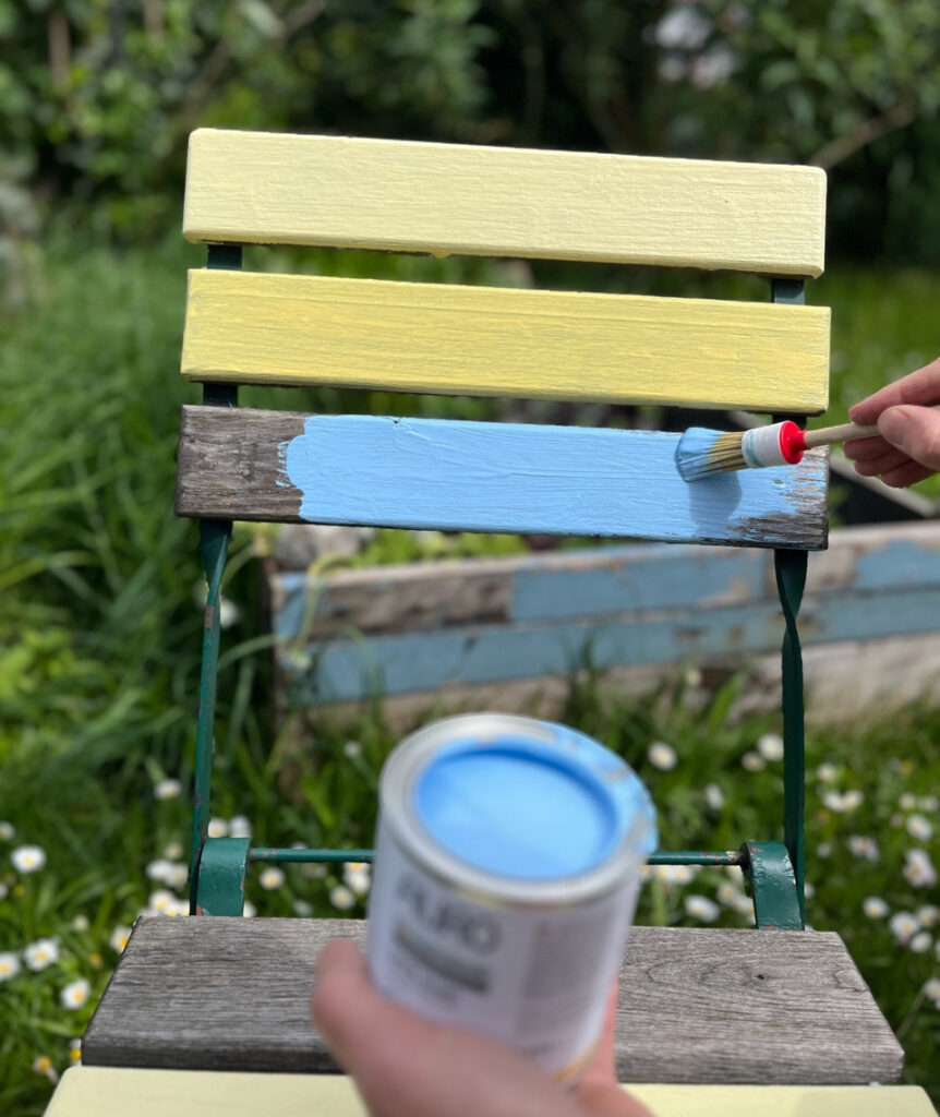 alter Gartenstuhl, der mit gelbem und blauem Lack gestrichen wird