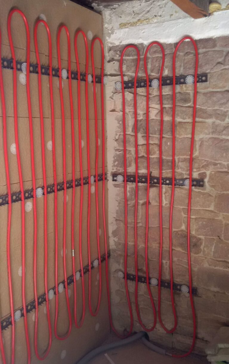 Zimmerecke mit rohen Wänden und Rohren für Wandheizung, rechte Wand aus Backsteinen