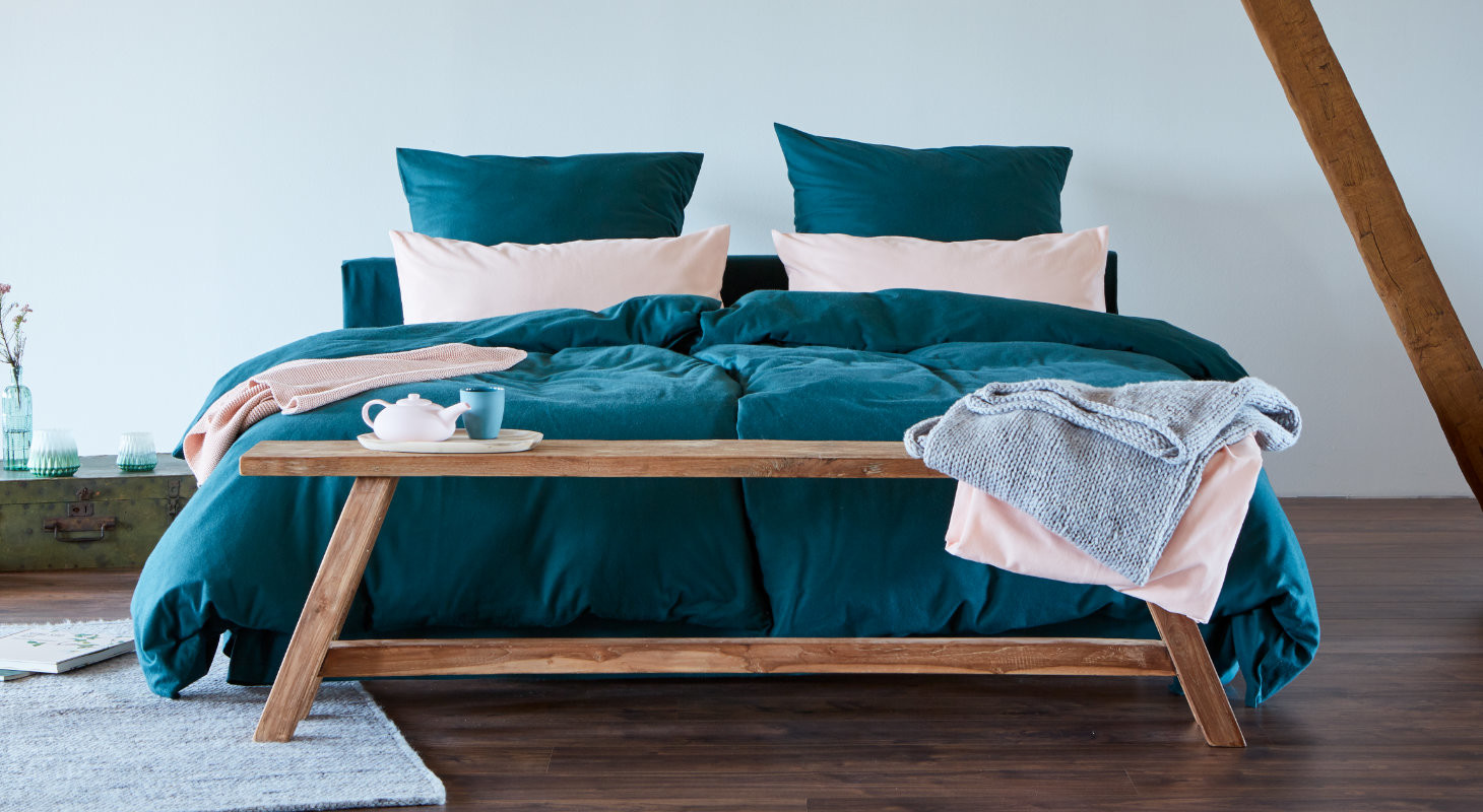 Bett mit blauer Bettwäsche und rosa Kissen