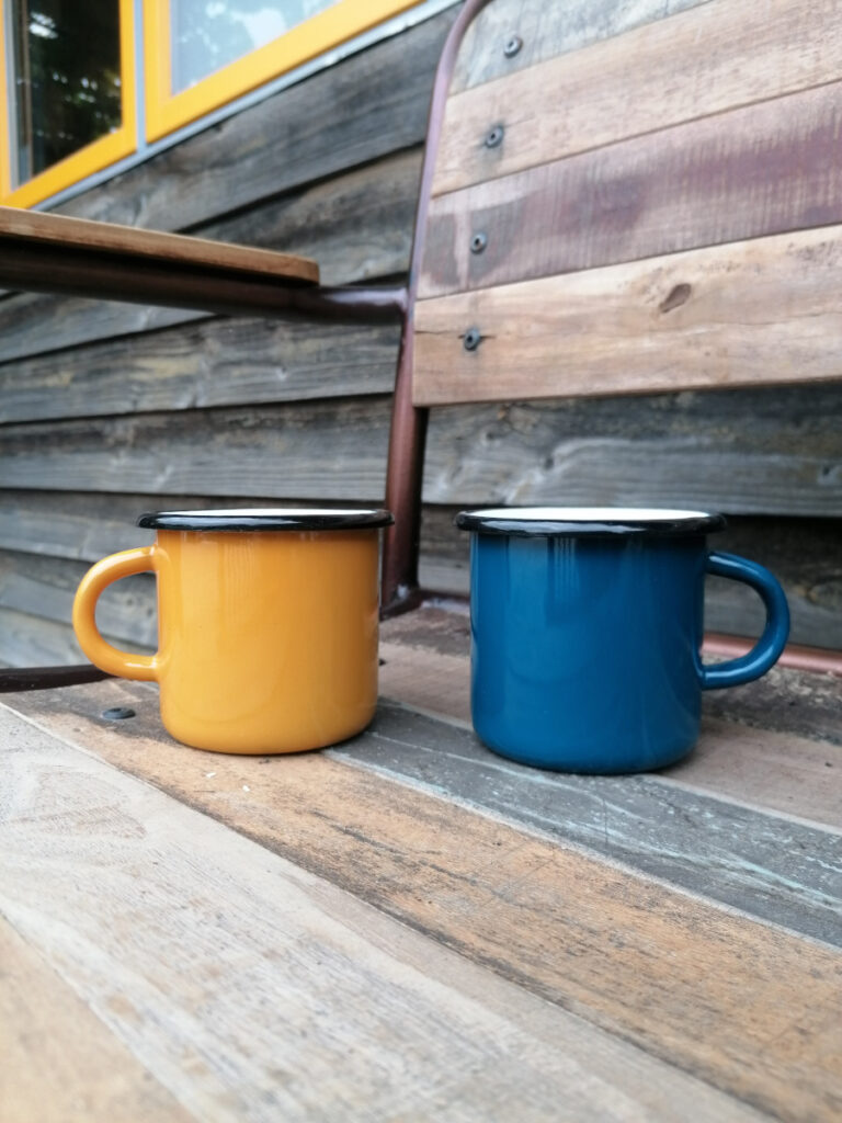 blaue und gelbe Emailtasse stehen draußen auf einem Stuhl