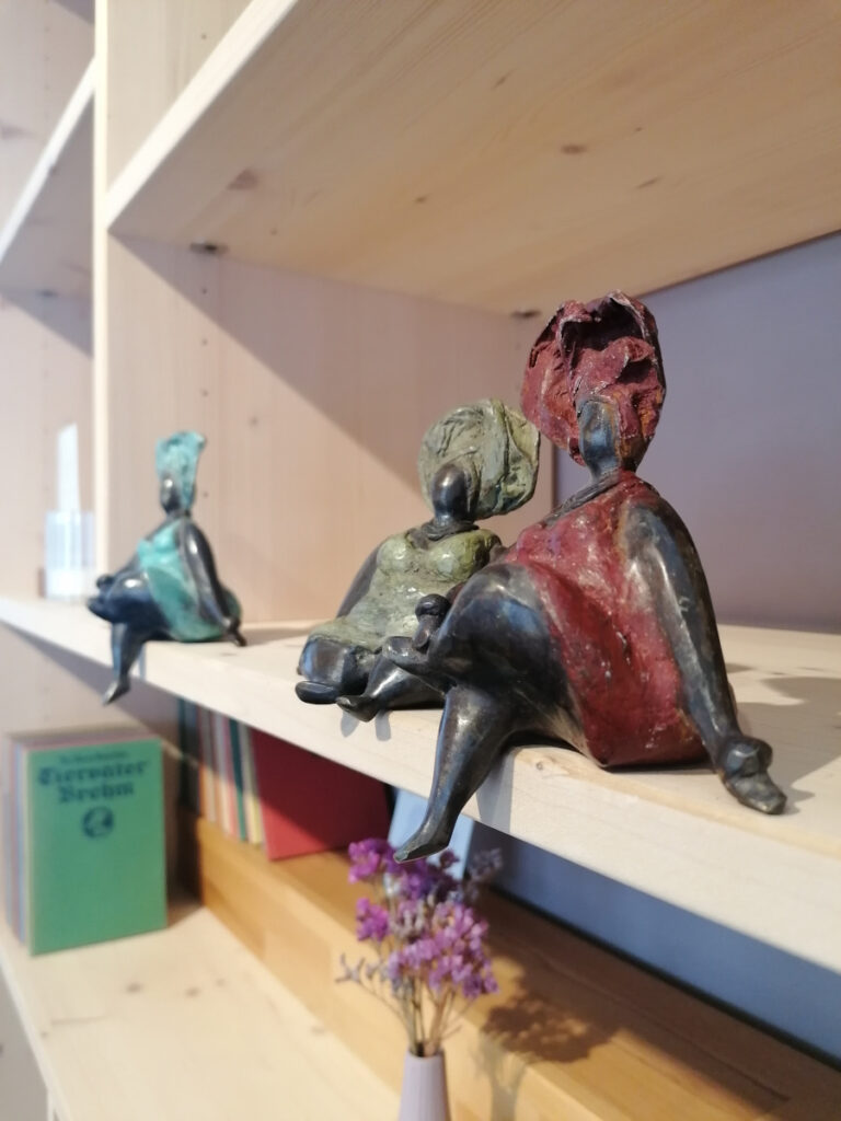 drei weibliche Bronzefiguren aus Afrika mit bunten Kleidern und Kopftüchern sitzen in einem Regal