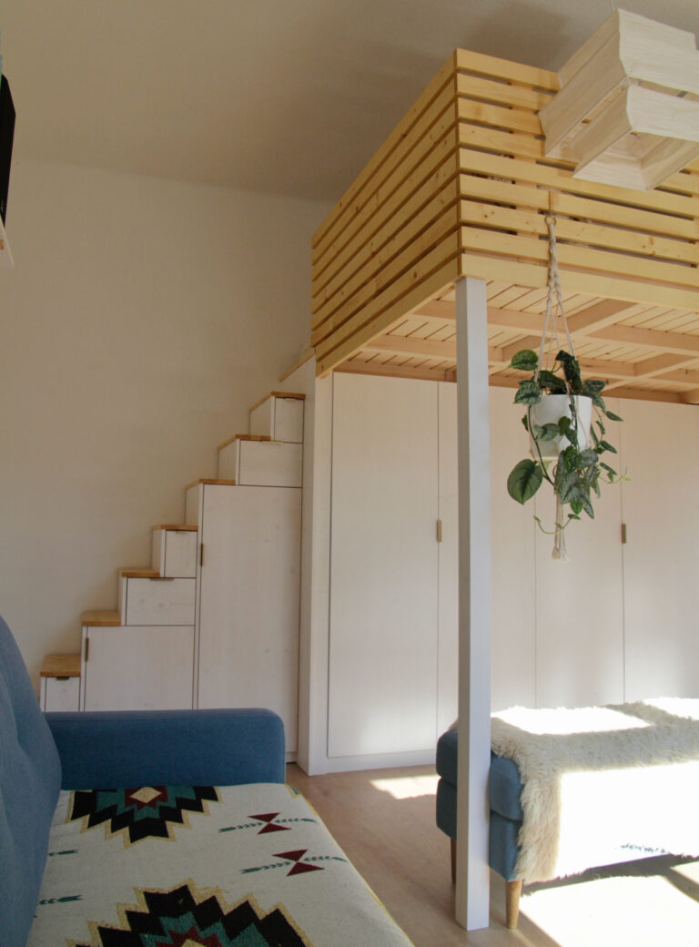Hochbett in hellem Holz. In die weiße Treppe, die zum Bett hoch führt, wurden Schubladen und Schrankfächer integriert