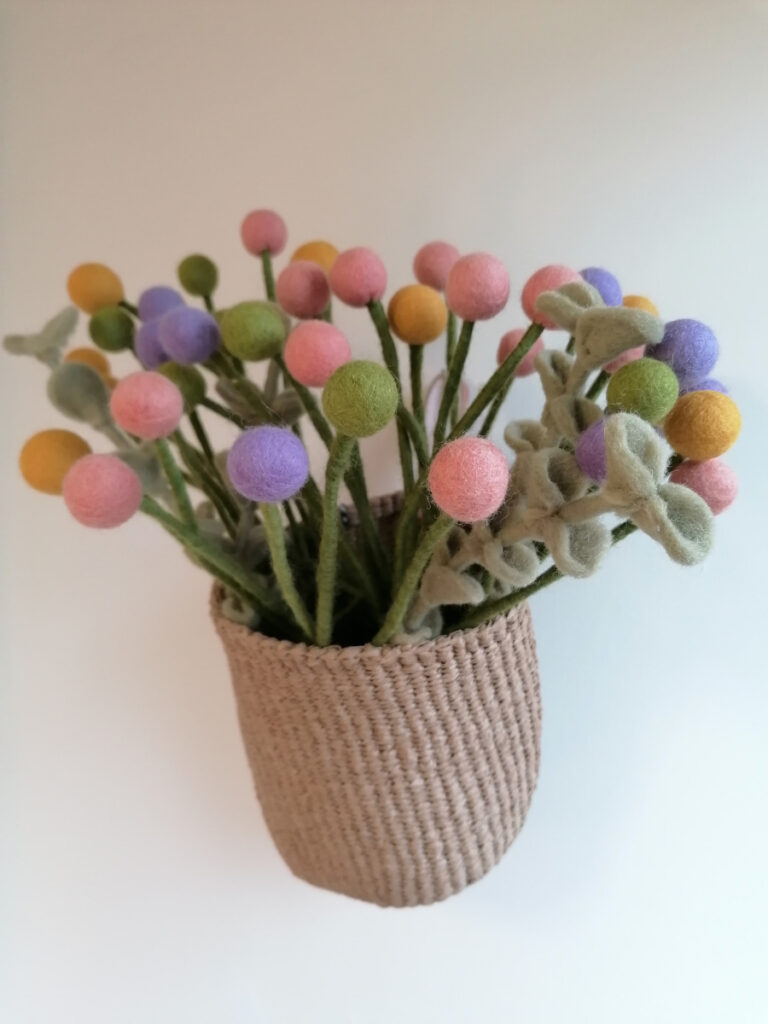 Korb mit Filzblumen hängt an der Wand