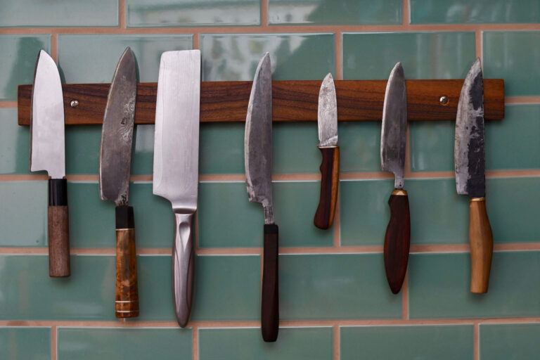 handgeschmiedete Messer hängen an einer Leiste vor einer türkis gefliesten Wand