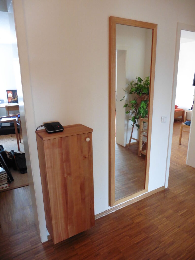 kleines Schränkchen und hoher Spiegel aus hellem Holz in einem Flur