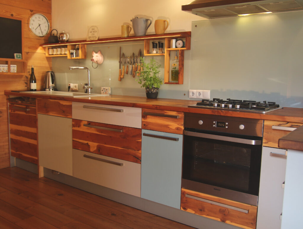 Glasplatte (rückseitig weiß lackiert) als Spritzschutz an der Wand Küche mit wild gemasertem Holz und bunten Fronten