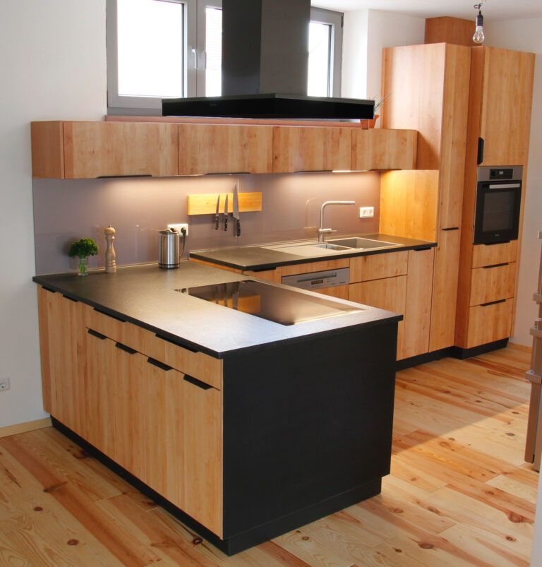 Eckküche aus hellem Holz mit schwarzer Arbeitsplatte und schwarzen Griffen