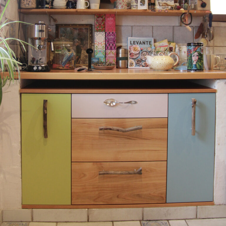 kleiner Einbauschrank in einer Küche mit bunten Fronten und einem Löffel als Schubladengriff