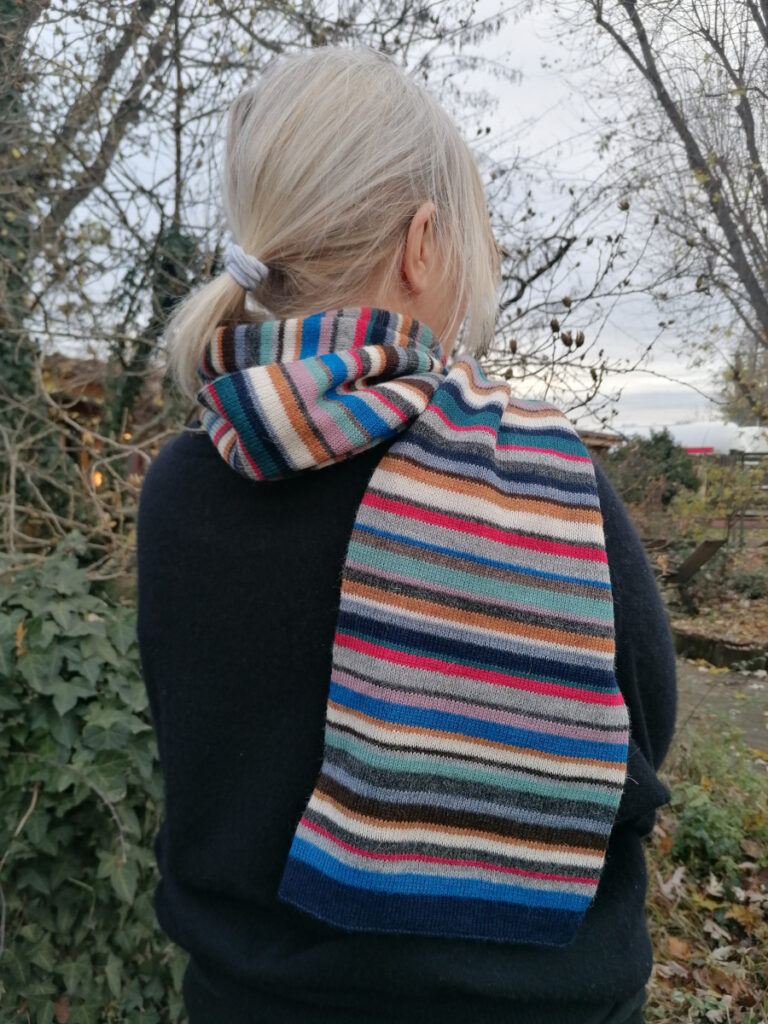 Frau mit blonden Haaren trägt einen bunt-gestreiften Wollschal
