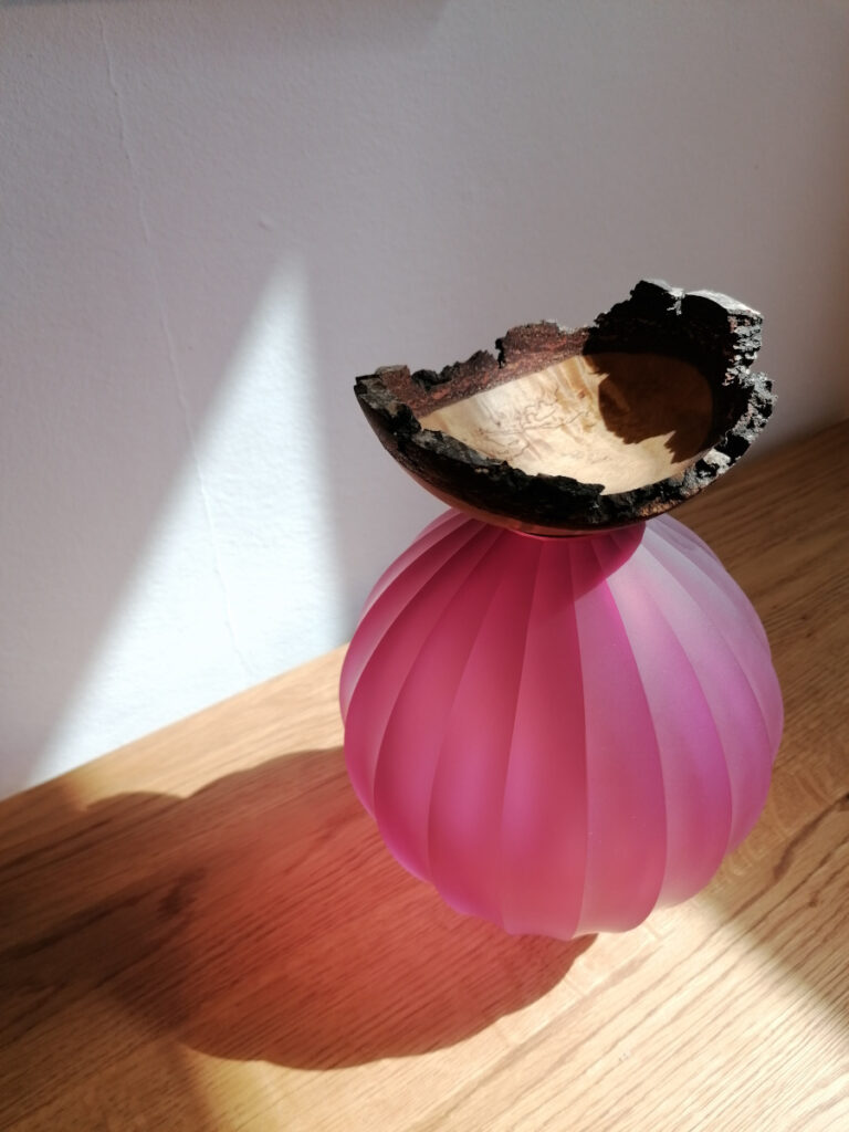 pinke Glasvase mit einem Deckel aus Holz, an dem die Rinde noch zu sehen ist