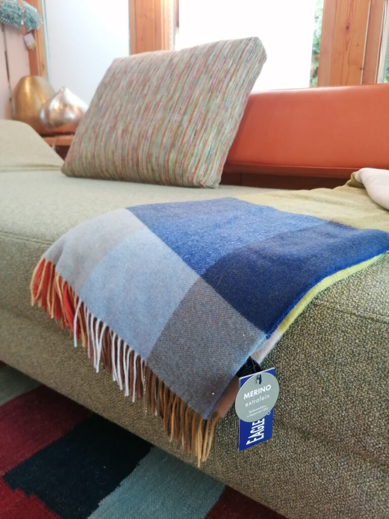 grünes Sofa, auf dem eine blaue Wolldecke liegt