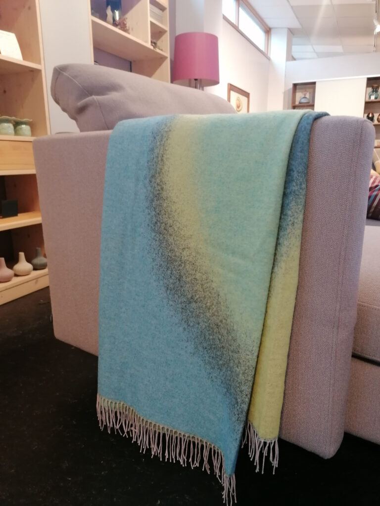 graues Sofa, über dem eine Wolldecke mit grün-blauem Muster hängt