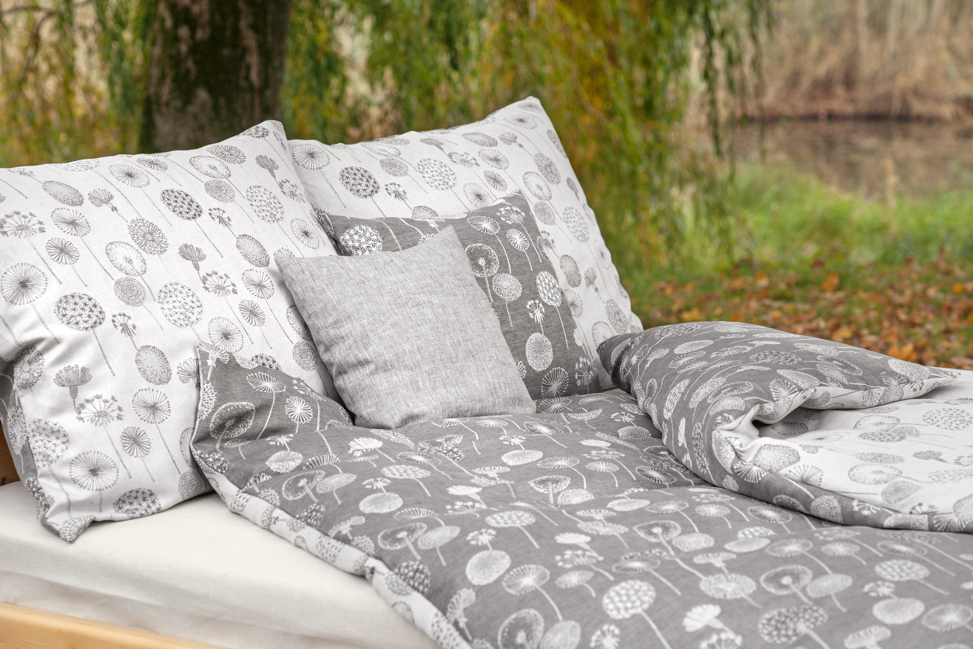 Bett mit silberfarbener Bettdecke und Kissen mit Pusteblumenmotiv
