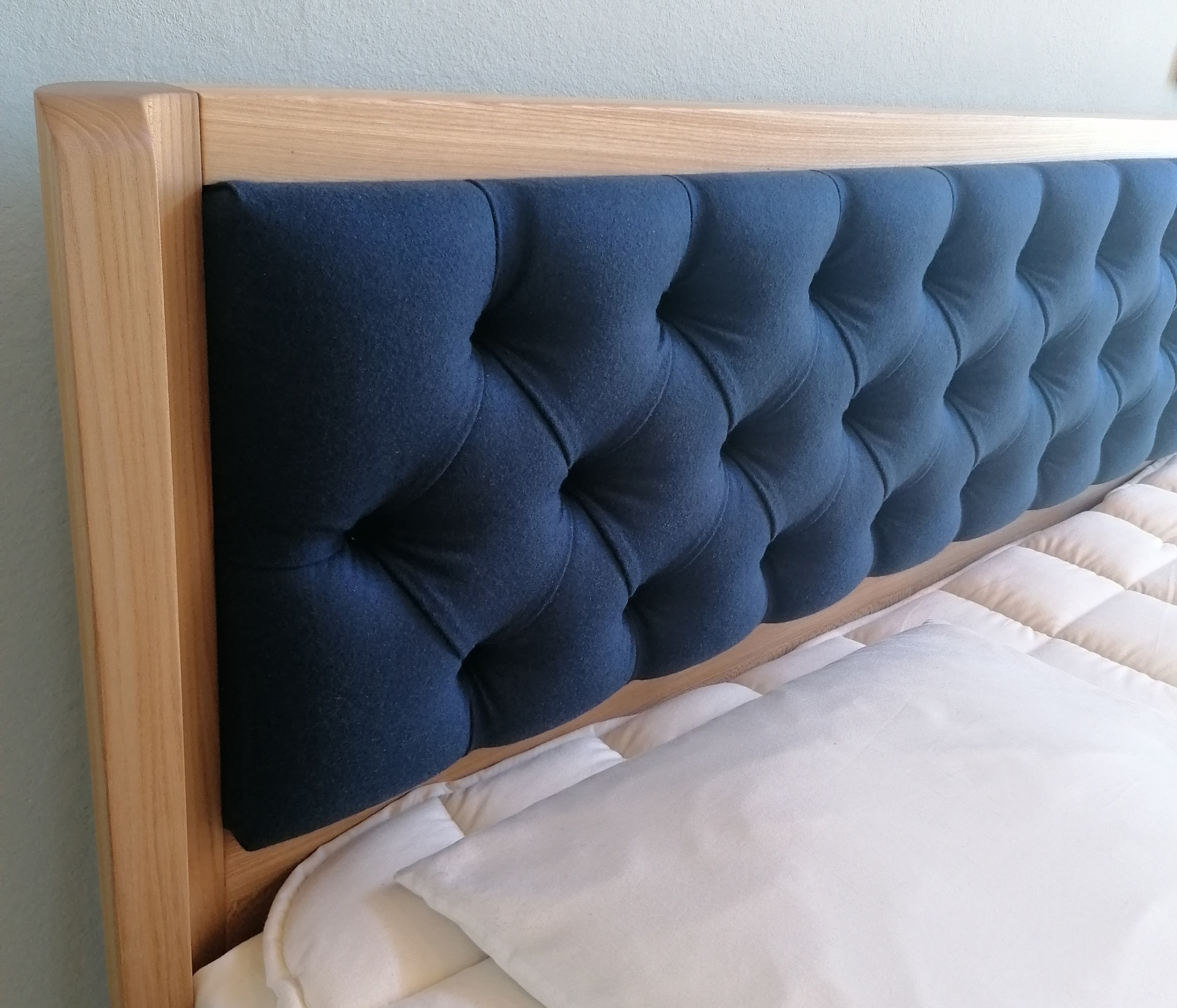 Kopfteil eines Holzbettes mit blauem Wollfilz