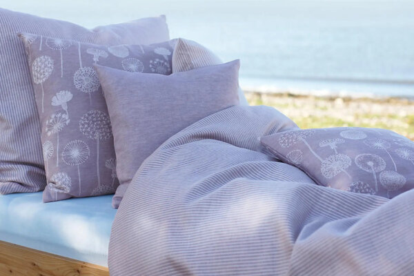 Bett, das an einem Strand steht mit fliederfarbener Bettdecke und Kissen